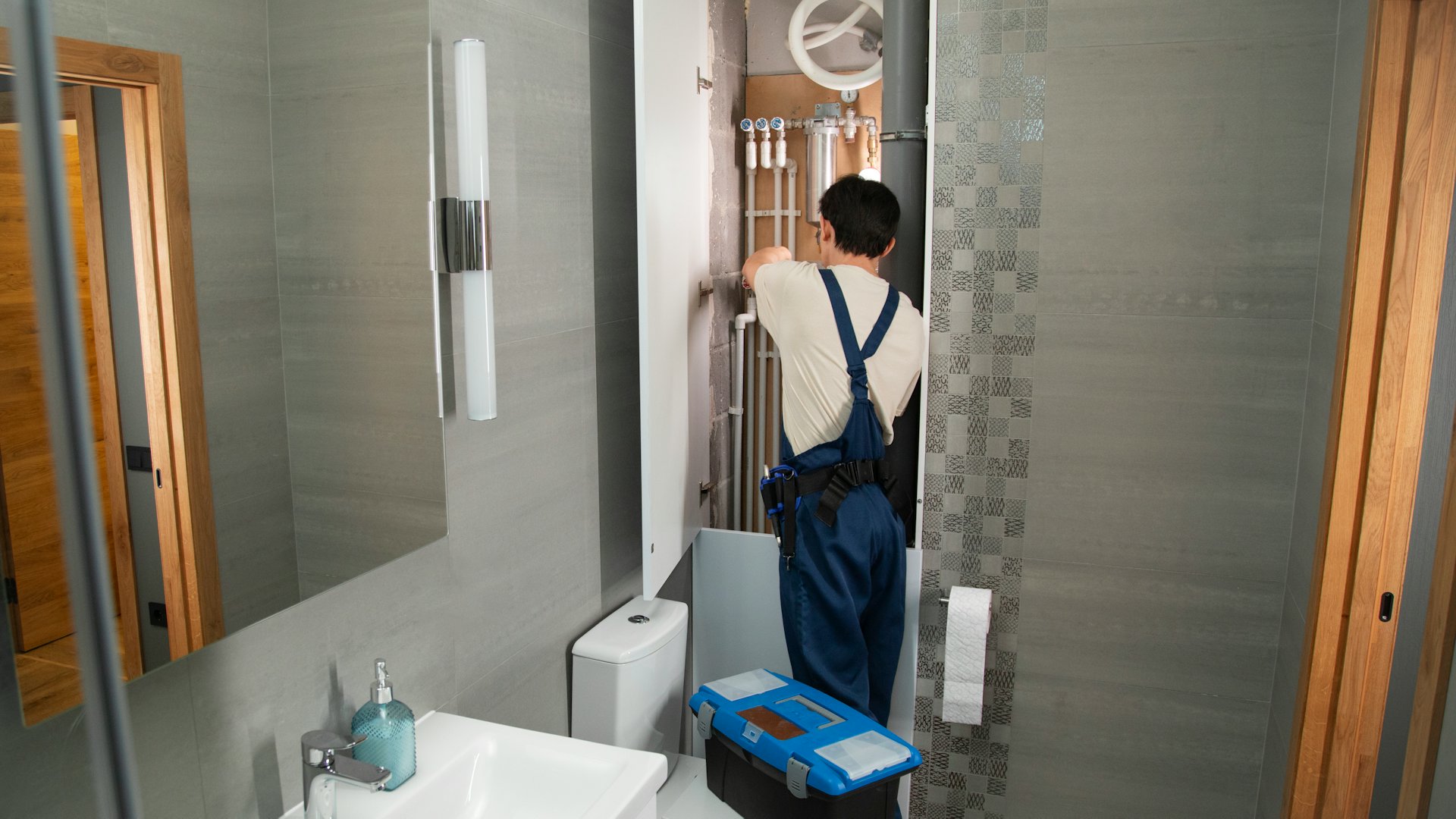 A plumber working on copper pipework beneath a bathroom fitting, tools laid out nearby.