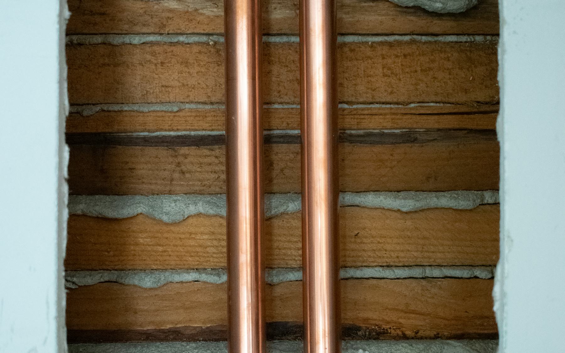 Close-up detail of two parallel copper pipes running through timber joists.