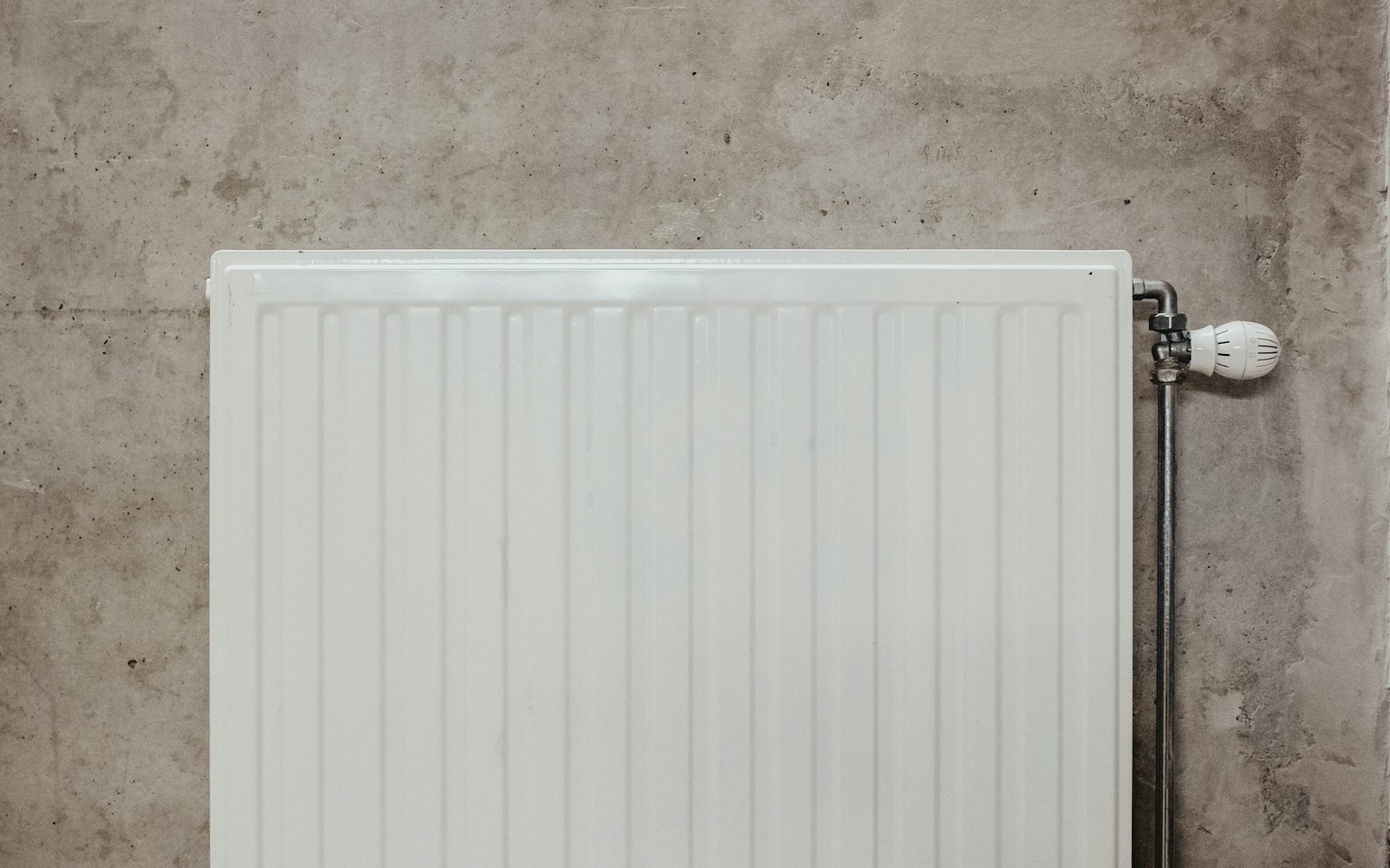 Wall-mounted radiator with copper pipe connection, neutral concrete wall.