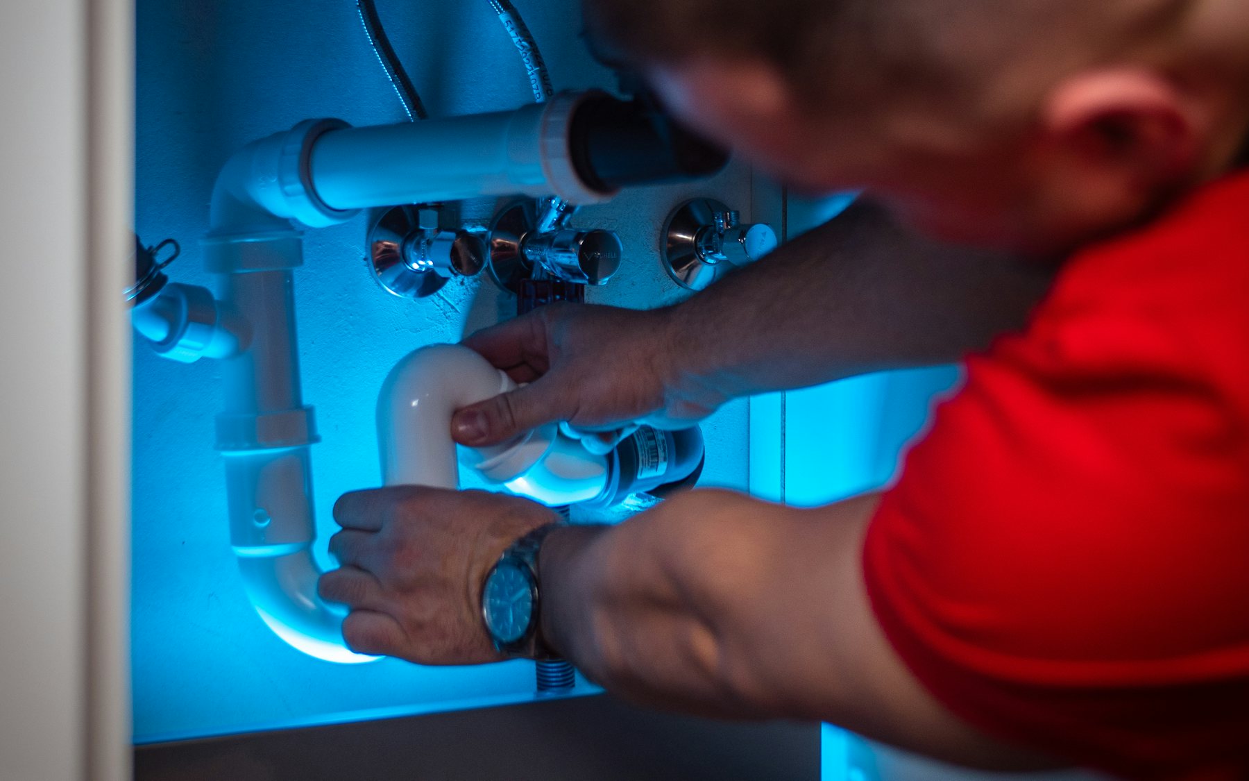 Plumber working beneath a kitchen sink connecting pipework and fittings.